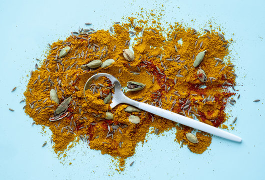 Various dry spices on a blue background, top view. Spices background. Mixed cardamom, cumin, curry, turmeric, paprika and hot peppers.