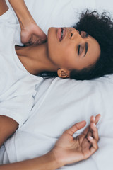 exhausted african american woman suffering from neck pain while lying in bed with closed eyes