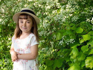 А pretty little girl is picking flowers. A sunny child in a straw hat is picking dandelions on a green glade. Summer girl.