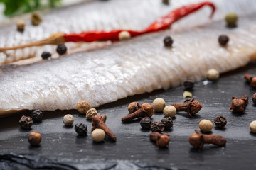Salted fillets of wild-caught Atlantic Herring garnished with Red Chili Pepper and Rainbow Peppercorns on black stone background. Clupea harengus.