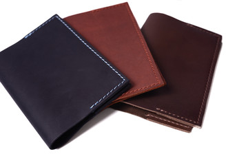 Three handmade leather passport covers isolated on white background. Closeup view. Covers are dark blue, red, brown and closed.
