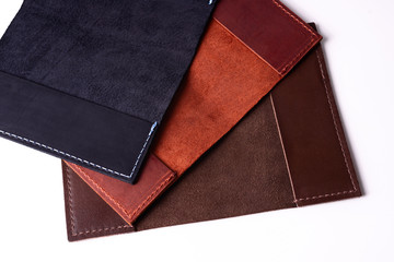 Three handmade leather passport covers isolated on white background. Closeup view. Covers are dark blue, red, brown and opened.