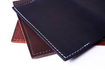 A parts of three handmade leather passport covers isolated on white background. Closeup view. Covers are dark blue, red and brown.