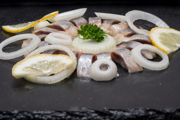 Hollandse Nieuwe- Traditional Dutch Food. Soused raw Herring soaked in mild marinade. Garnished with Lemon, Onion and Parsley on black natural stone.