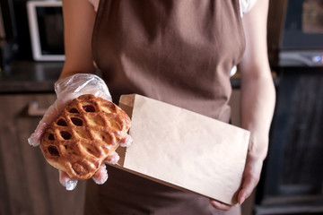 European woman sells in bakery putting sweet pie in paper bag. Small business concept