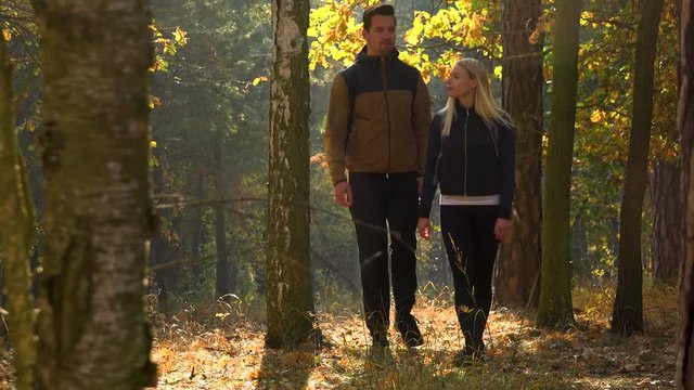 A hiking couple walks through a forest on a sunny day - front view