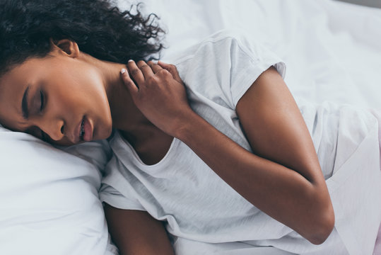 attractive african american woman suffering from neck pain while lying in bed with closed eyes