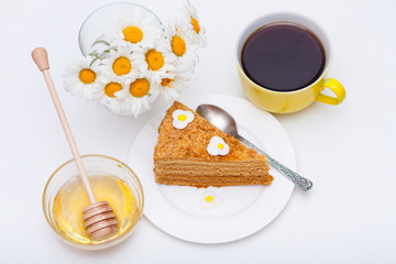 Slice of homemade layers honey cake with yellow cup of tea or coffee and chamomiles.