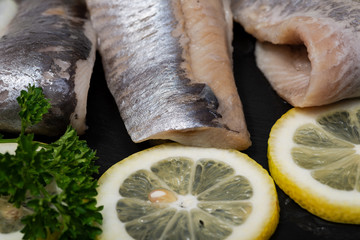 Salted Deboned Herring Fillets garnished with Yellow Onion, Lemon and Fresh Parsley. Natural black stone background. Clupea harengus.