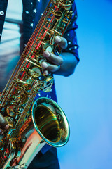 Young african-american jazz musician playing the saxophone on blue studio background in trendy neon...