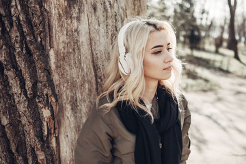 Beautiful Blonde Girl in Green Jacket Listening Music in Headphones