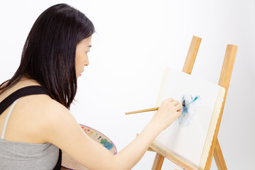 Asian American artist painting on an easel