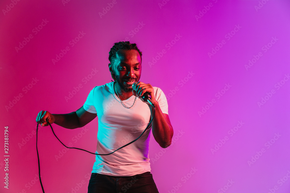 Wall mural young african-american jazz musician with microphone singing a song on purple studio background in t