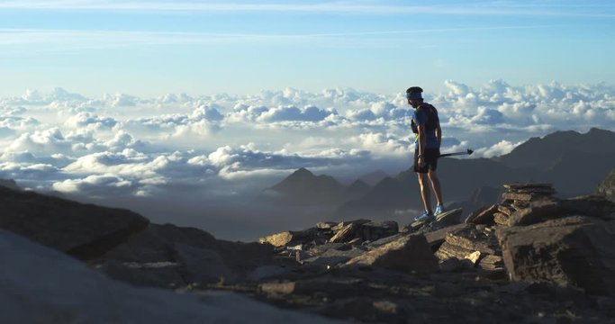 Trail runner man running reaching mountain top peak goal looking horizon view.Wide shot.Wild nature outdoors at sunrise or sunset backlit.Training activity,sport,effort,challenge,willpower concepts