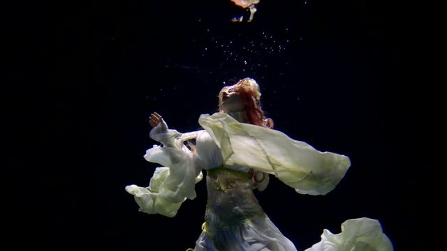 Incredible woman dressed like underwater princess posing in darkness. Exotic woman floating in a dark pool