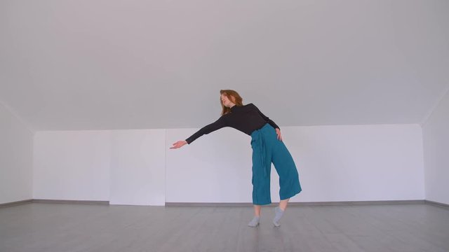 Motion shoot of young beautiful skilled female performing an emotional dance gracefully in the room indoors