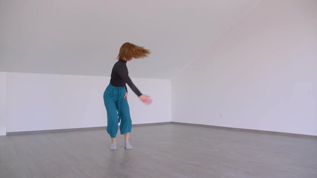 Motion shoot of young beautiful skilled female performing an emotional dance in the room indoors in a flat