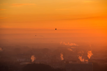 Sunrise over factory at the industrial area. Orange light rays comes through morning fog and smoke from pipes. Industrial chemical manufacturing