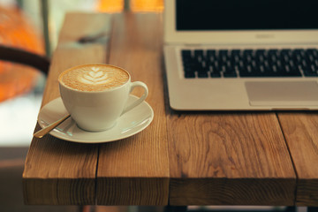Horizontal photo of cup of latte and modern laptop