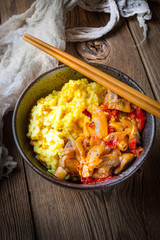 Saffron rice with pieces of chicken and vegetables on wooden table.