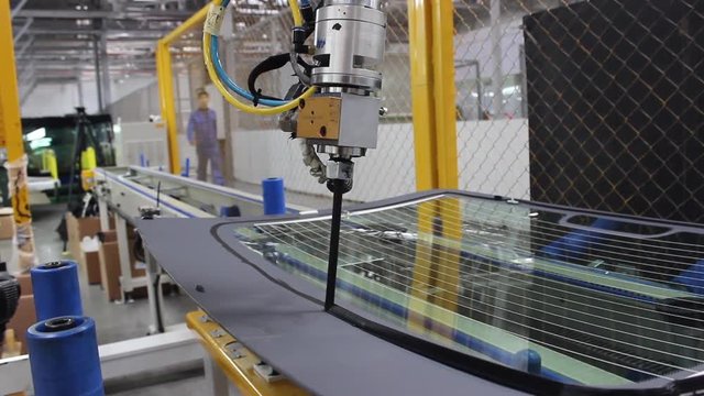 The robot, on the assembly line of the automobile plant, applies glue to the automotive glass.