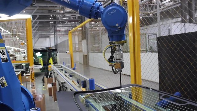 The robot, on the assembly line of the automobile plant, applies glue to the automotive glass.