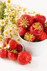 Scattered strawberry berry and in a small bucket on a light background with a bouquet of chamomile flowers . Summer berry season.