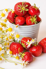 Scattered strawberry berry and in a small bucket on a light background with a bouquet of chamomile flowers . Summer berry season.