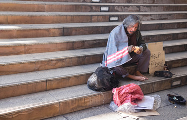 Homeless man is sitting down on staircase and walkway in town.He is eating bread.He is very unhappy. poverty,despair, Photo Sympathetic and hope concept.