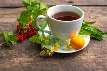 white cup with tea on a wooden table, around a berry, strawberry, mint