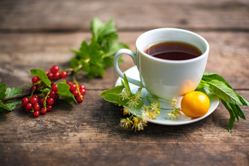 white cup with tea on a wooden table, around a berry, strawberry, mint