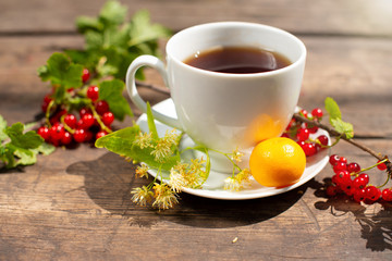 white cup with tea on a wooden table, around a berry, strawberry, mint