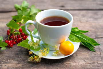 white cup with tea on a wooden table, around a berry, strawberry, mint