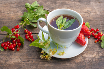 white cup with tea on a wooden table, around a berry, strawberry, mint
