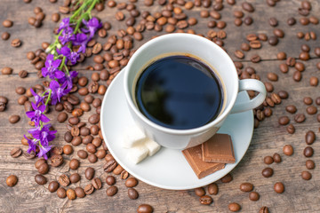 white cup of coffee on a wooden table, chocolate, sugar and coffee beans,