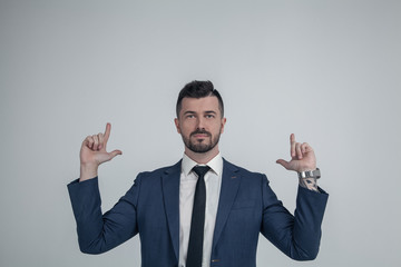 Confident young Caucasian man point with finger looking up demonstrating good advertising sale offer, excited European male in spectacles isolated on grey studio background show upward.Dressed in suit