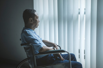 Sad old man looks out the window in wheelchair