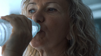 senior woman drinks water from drinking water in the gym, close up