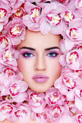 Young beautiful tanned sexy woman with fancy make-up and pink orchids around her face