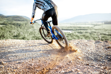 Professional well-equipped cyclist riding extremely on the rocky mountains raising dust behind during the sunset