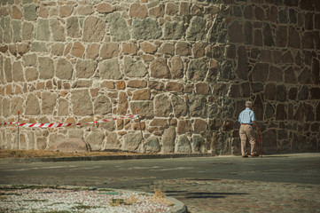 Old man walking in front of the thick city wall of Avila