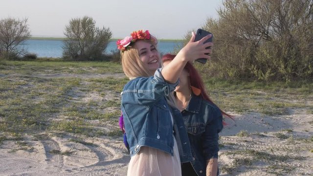Two young woman making a selfie in backdrop of the sandy beach and lake