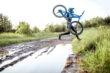 Professional well-equipped cyclist jumping through the puddle on the mountain dirt road during the sunset