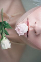top view of beautiful woman lying in clear water with rose in mouth
