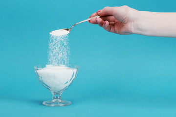 partial view of woman adding granulated sugar into glass bowl on blue background