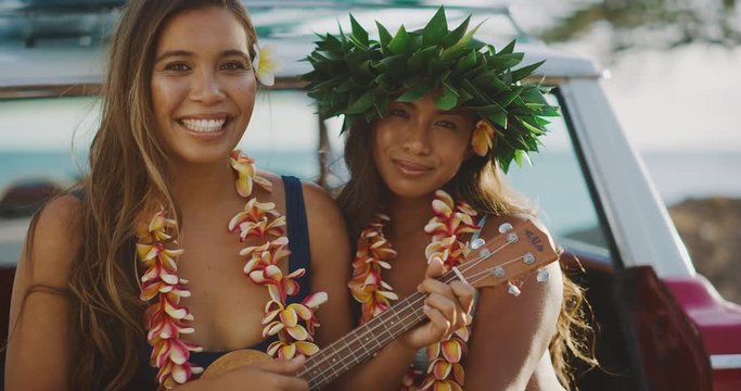 Portrait of beautiful young women singing smiling and playing the ukulele, sitting in a vintage beach cruiser car at sunset, happy laughing women wearing flower leis, hawaiian island cruising