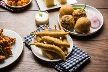Indian Tea time snacks  in group includes Veg Samosa, Kachori/kachaudi, aloo bonda, khaman dhokla, bread, onion,chilli and moong pakora/pakoda/bhaji/bhajji/Bhajiya/bajji with sauces, selective focus