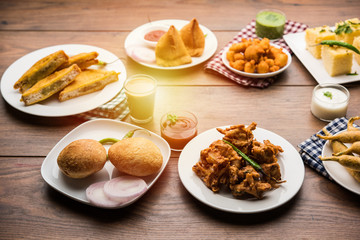 Indian Tea time snacks  in group includes Veg Samosa, Kachori/kachaudi, aloo bonda, khaman dhokla, bread, onion,chilli and moong pakora/pakoda/bhaji/bhajji/Bhajiya/bajji with sauces, selective focus