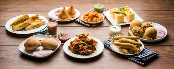 Indian Tea time snacks  in group includes Veg Samosa, Kachori/kachaudi, aloo bonda, khaman dhokla, bread, onion,chilli and moong pakora/pakoda/bhaji/bhajji/Bhajiya/bajji with sauces, selective focus