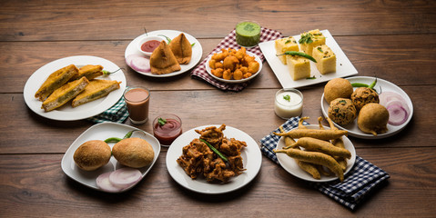 Indian Tea time snacks  in group includes Veg Samosa, Kachori/kachaudi, aloo bonda, khaman dhokla, bread, onion,chilli and moong pakora/pakoda/bhaji/bhajji/Bhajiya/bajji with sauces, selective focus